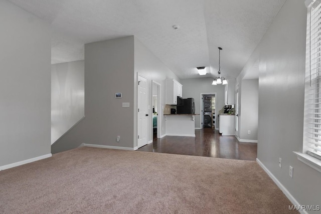 unfurnished living room featuring a textured ceiling, a notable chandelier, and dark carpet