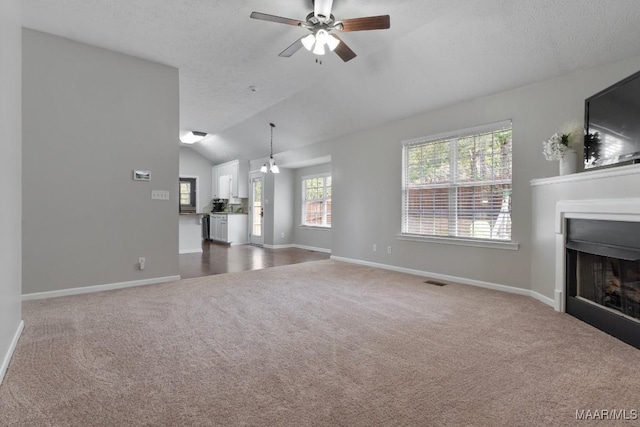 unfurnished living room with a textured ceiling, vaulted ceiling, ceiling fan, and carpet flooring