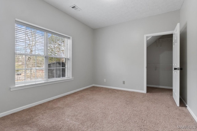 unfurnished bedroom featuring a walk in closet, light carpet, a textured ceiling, and a closet