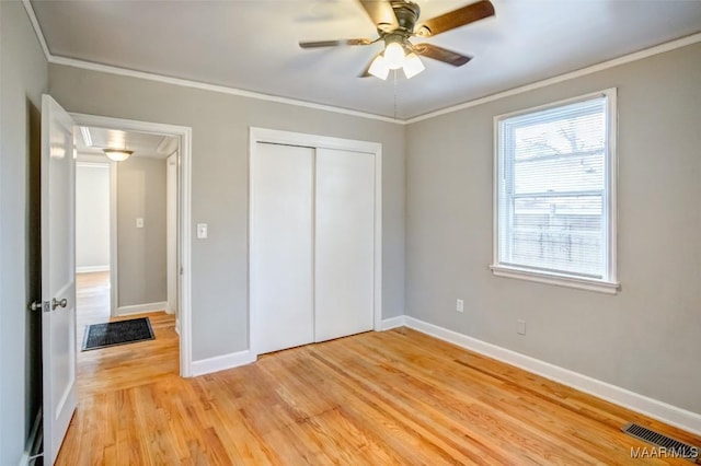 unfurnished bedroom featuring ornamental molding, ceiling fan, light wood-type flooring, and a closet