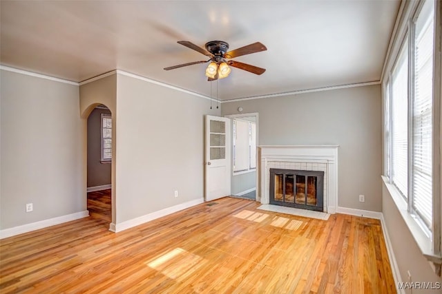 unfurnished living room featuring a tiled fireplace, ornamental molding, ceiling fan, and light hardwood / wood-style floors