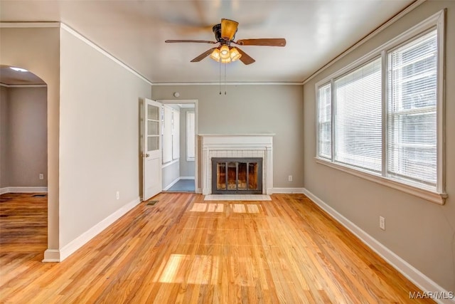 unfurnished living room featuring crown molding, ceiling fan, a tile fireplace, and light hardwood / wood-style flooring