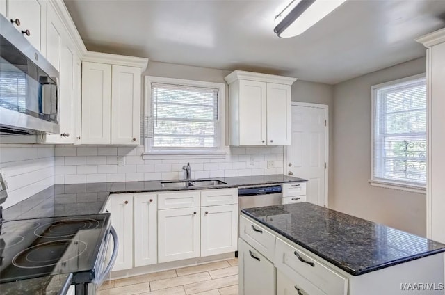 kitchen with white cabinetry, sink, dark stone counters, decorative backsplash, and stainless steel appliances