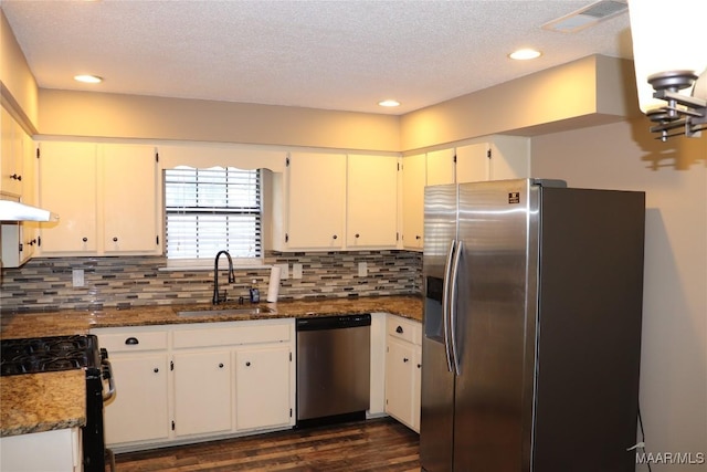 kitchen with stainless steel appliances, white cabinetry, sink, and dark stone counters