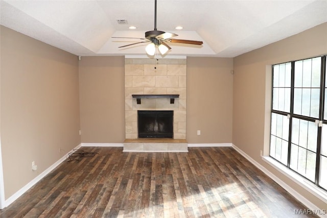 unfurnished living room with a fireplace, dark wood-type flooring, a raised ceiling, and a healthy amount of sunlight