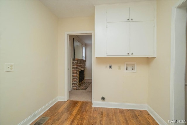 clothes washing area featuring hardwood / wood-style flooring, electric dryer hookup, hookup for a washing machine, cabinets, and a fireplace