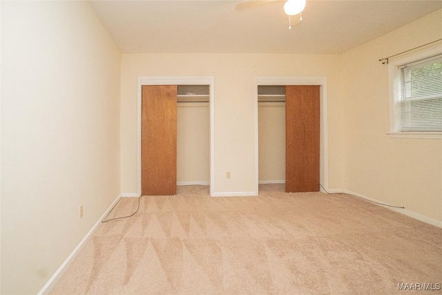 unfurnished bedroom featuring multiple closets, light colored carpet, and ceiling fan