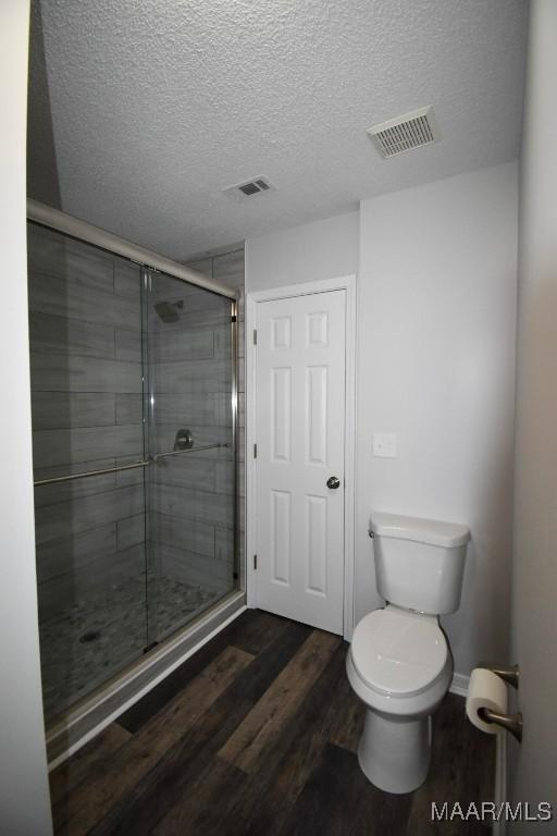 6515 Redland Rd, Wetumpka, AL 36093 - bathroom with a stall shower, a textured ceiling, toilet, visible vents, and wood finished floors