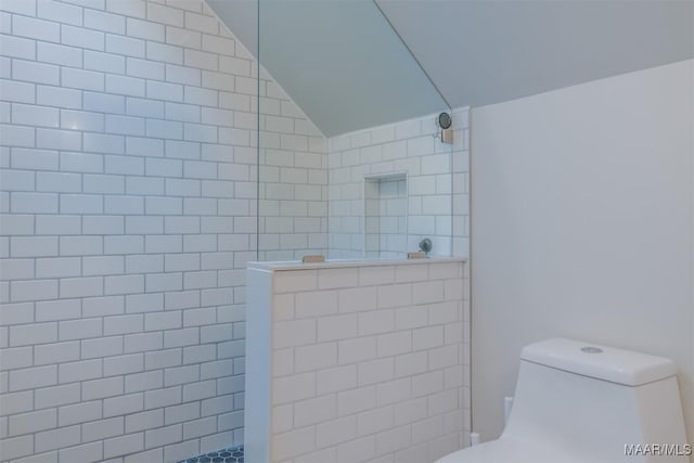 bathroom featuring lofted ceiling, toilet, and tiled shower