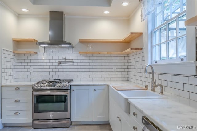 kitchen with wall chimney exhaust hood, sink, stainless steel gas stove, white cabinetry, and light stone countertops