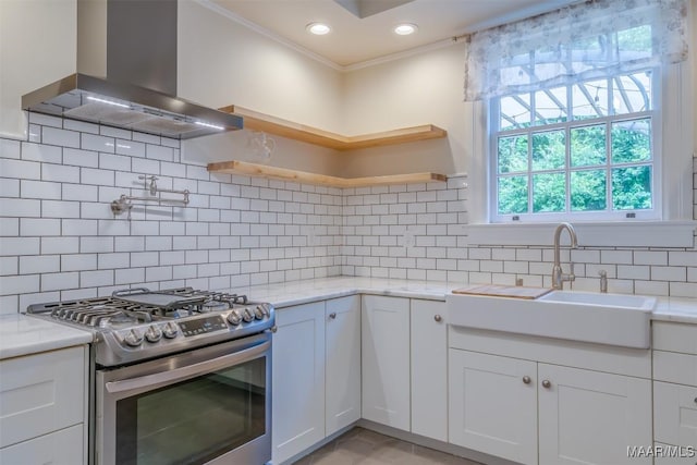 kitchen with sink, white cabinetry, light stone counters, stainless steel range with gas cooktop, and wall chimney range hood