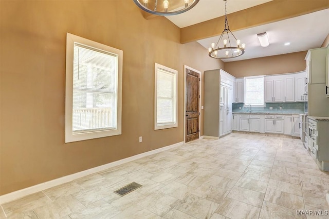 kitchen featuring an inviting chandelier, tasteful backsplash, pendant lighting, beam ceiling, and white cabinets