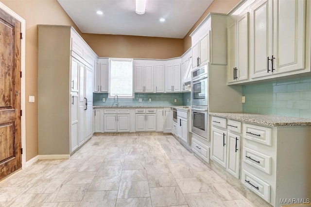 kitchen featuring light stone countertops, sink, white cabinets, and decorative backsplash