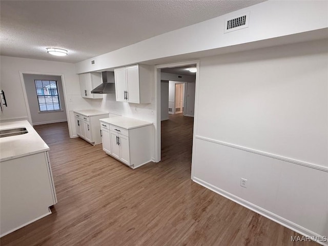 kitchen with sink, wood-type flooring, white cabinets, a textured ceiling, and wall chimney exhaust hood