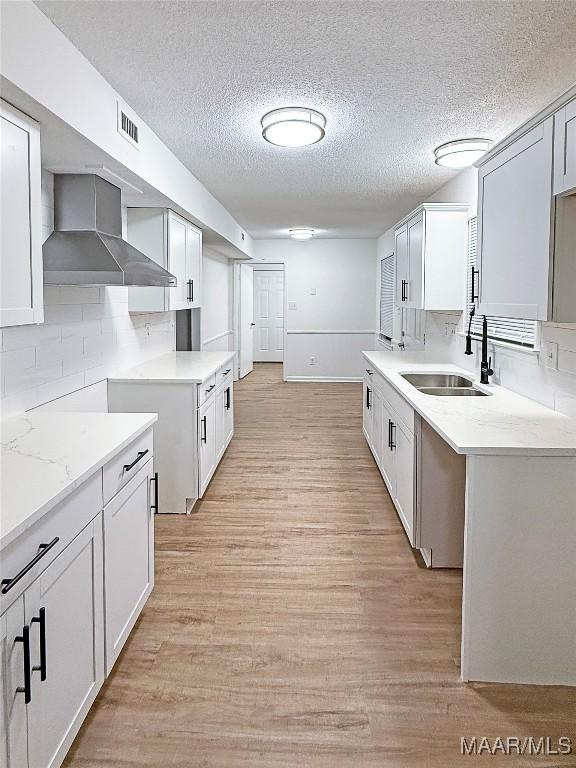 kitchen with white cabinetry, wall chimney range hood, and sink