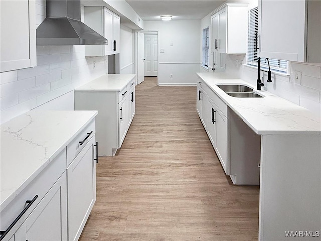 kitchen featuring sink, white cabinets, wall chimney exhaust hood, and light wood-type flooring