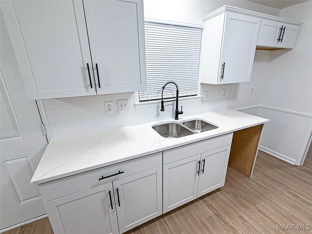 kitchen with white cabinetry, light stone countertops, sink, and light wood-type flooring