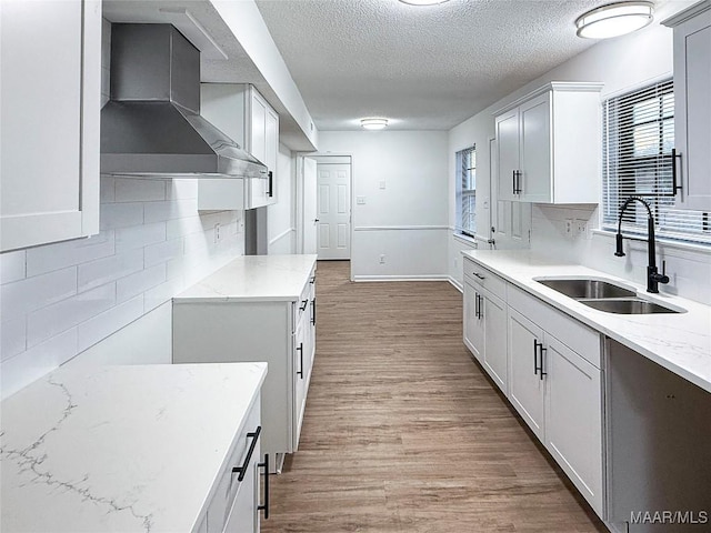 kitchen featuring sink, white cabinets, light hardwood / wood-style floors, light stone countertops, and wall chimney range hood