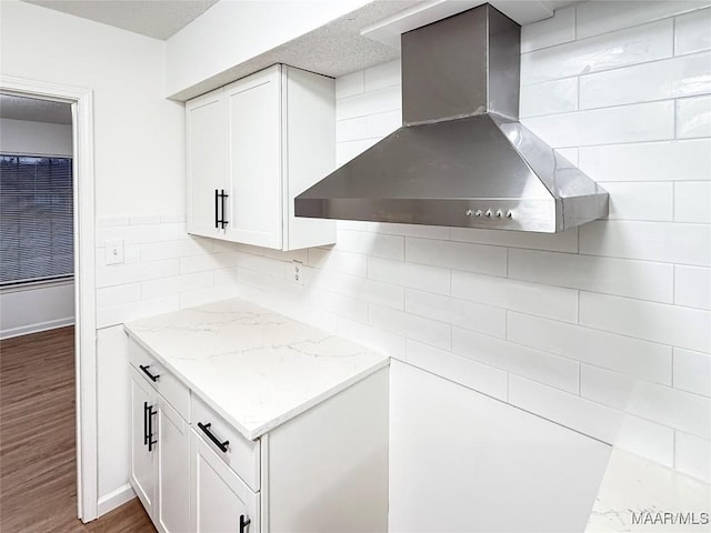 kitchen with backsplash, light stone countertops, white cabinets, dark hardwood / wood-style flooring, and wall chimney exhaust hood