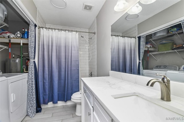 bathroom with separate washer and dryer, vanity, toilet, electric water heater, and a textured ceiling