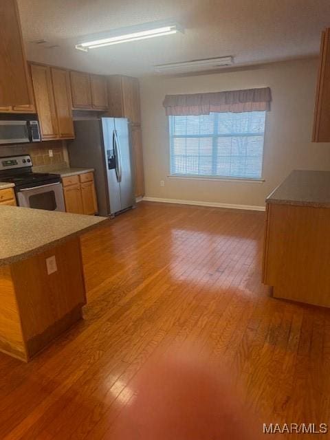 kitchen with appliances with stainless steel finishes, light hardwood / wood-style flooring, and backsplash