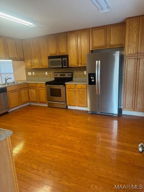 kitchen with appliances with stainless steel finishes, sink, decorative backsplash, and light wood-type flooring