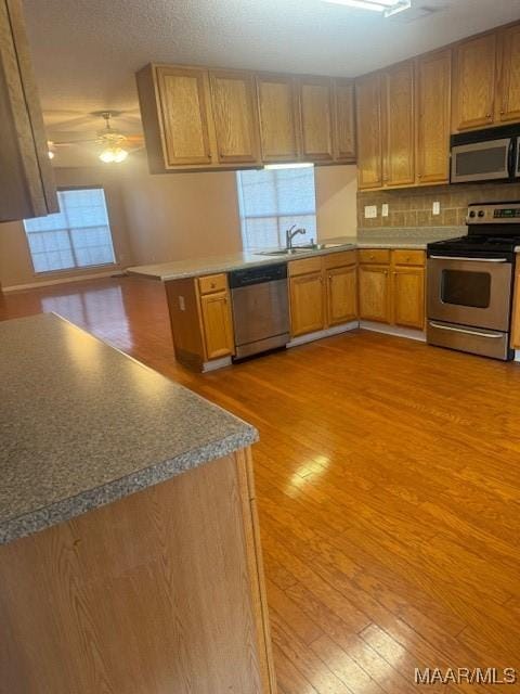 kitchen featuring stainless steel appliances, a peninsula, a sink, a ceiling fan, and light wood finished floors