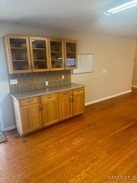 bar featuring dark wood-style flooring, backsplash, and baseboards