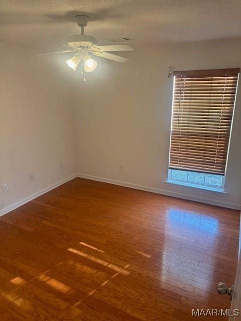 empty room with a textured ceiling, wood finished floors, a ceiling fan, and baseboards