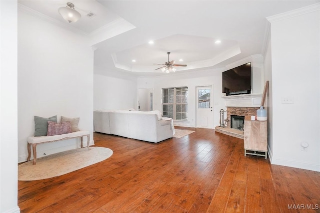 living room with crown molding, a raised ceiling, hardwood / wood-style flooring, ceiling fan, and a fireplace