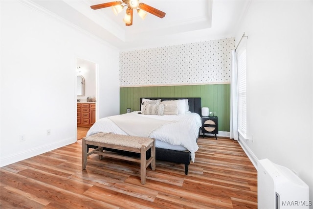 bedroom featuring connected bathroom, wood-type flooring, ornamental molding, ceiling fan, and a raised ceiling