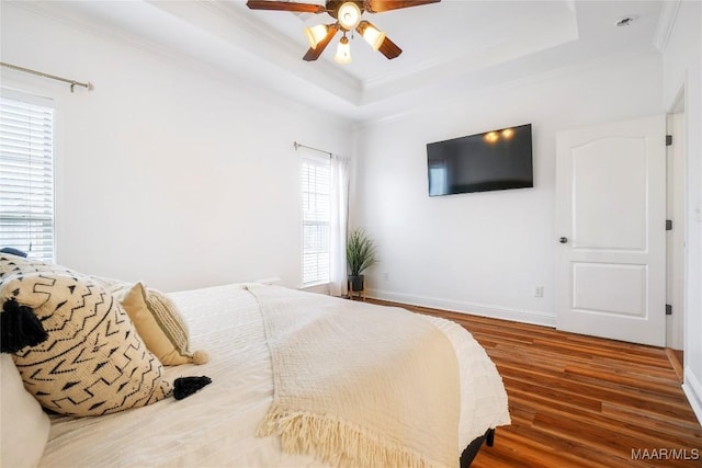 bedroom featuring dark wood-type flooring, ceiling fan, ornamental molding, and a raised ceiling