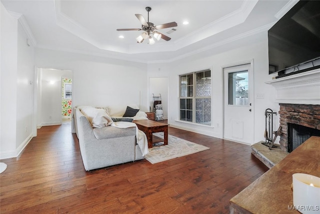 living room with a tray ceiling, a fireplace, ornamental molding, and dark wood-type flooring