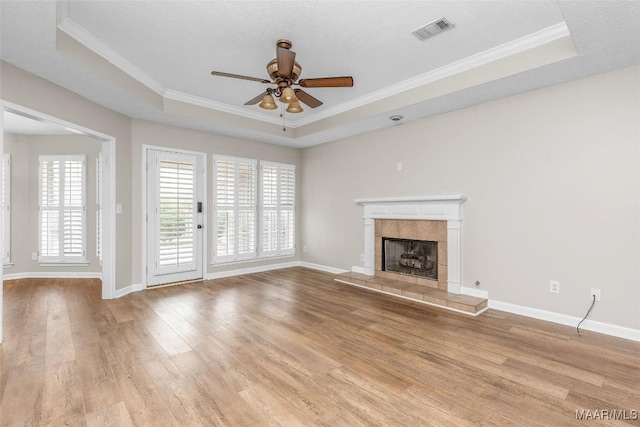 unfurnished living room featuring crown molding, ceiling fan, a fireplace, light hardwood / wood-style floors, and a raised ceiling