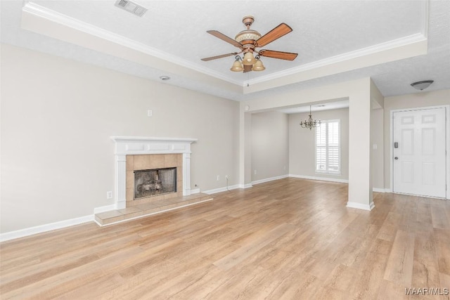 unfurnished living room featuring a tiled fireplace, ornamental molding, a raised ceiling, and light hardwood / wood-style flooring