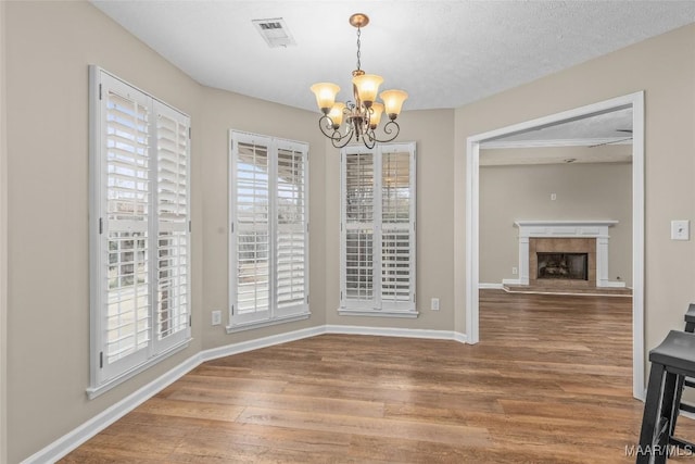 dining room featuring an inviting chandelier, wood-type flooring, a tile fireplace, and a textured ceiling