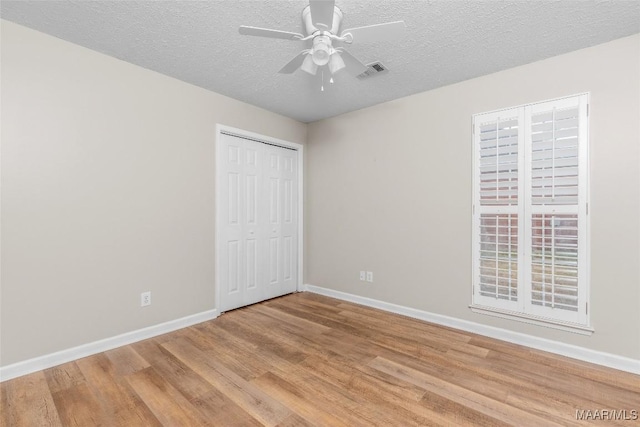 unfurnished bedroom featuring ceiling fan, a closet, a textured ceiling, and light wood-type flooring