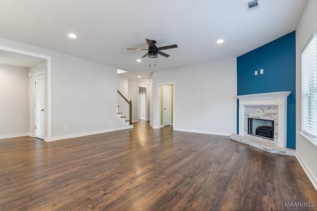 unfurnished living room with a stone fireplace, dark wood-type flooring, and ceiling fan