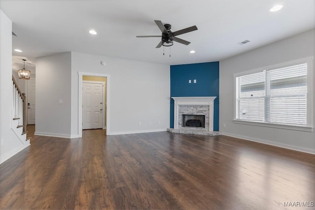 unfurnished living room with a stone fireplace, dark wood-type flooring, and ceiling fan with notable chandelier