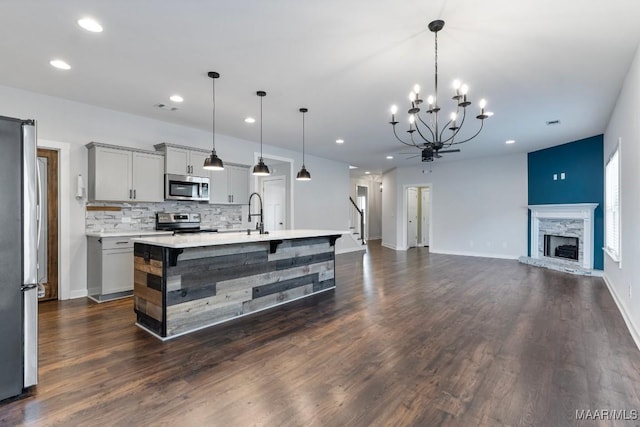 kitchen with gray cabinets, appliances with stainless steel finishes, a kitchen island with sink, and pendant lighting