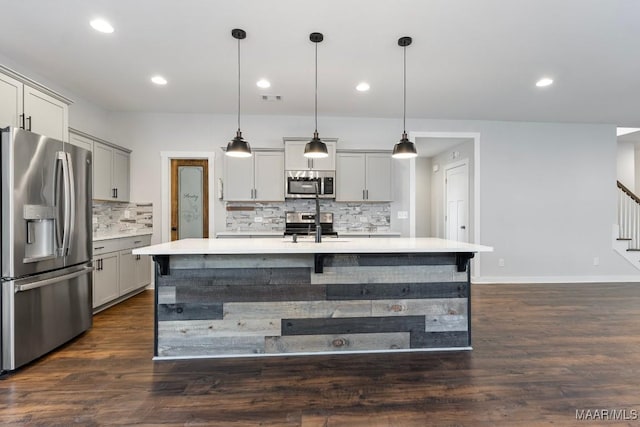 kitchen with sink, dark wood-type flooring, hanging light fixtures, stainless steel appliances, and a center island with sink