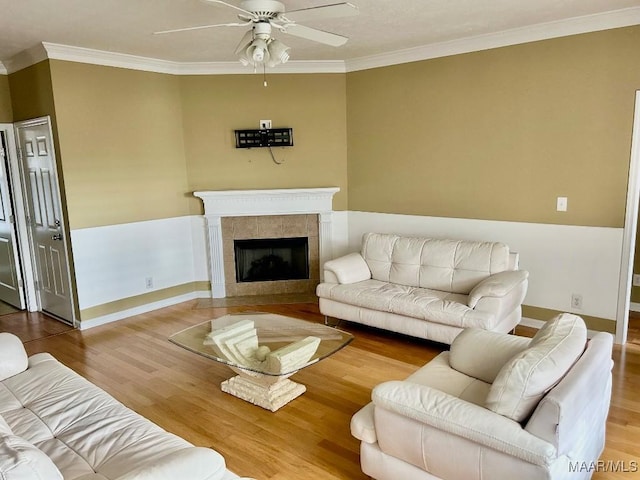 living room featuring crown molding, ceiling fan, hardwood / wood-style floors, and a tile fireplace