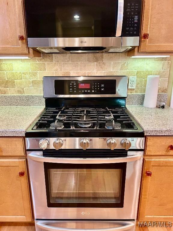 kitchen featuring light stone counters, backsplash, and stainless steel appliances