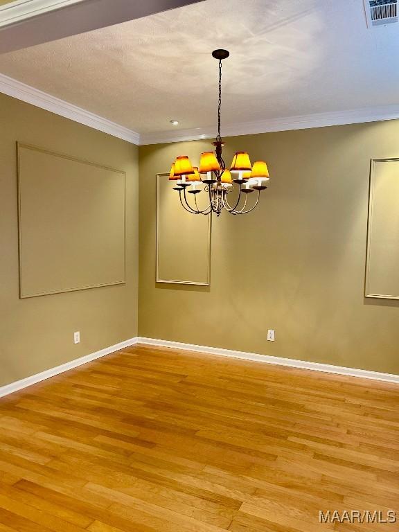 unfurnished dining area with crown molding, an inviting chandelier, and hardwood / wood-style floors