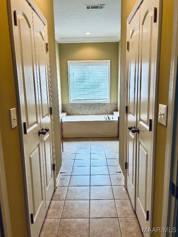 hall featuring light tile patterned flooring, a textured ceiling, and crown molding