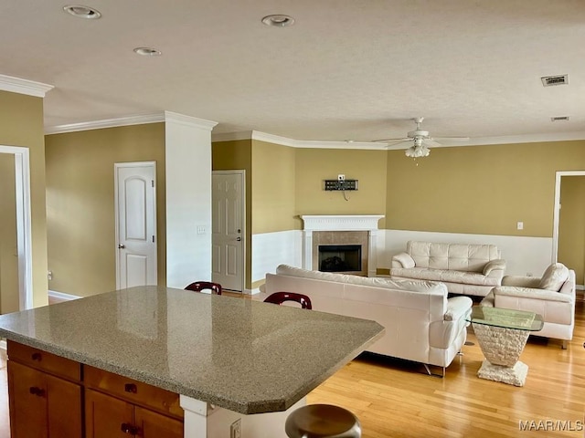 living room featuring crown molding, ceiling fan, a tile fireplace, and light wood-type flooring