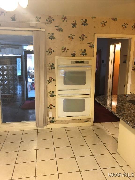 kitchen with light tile patterned floors, white double oven, dark stone counters, and white cabinets