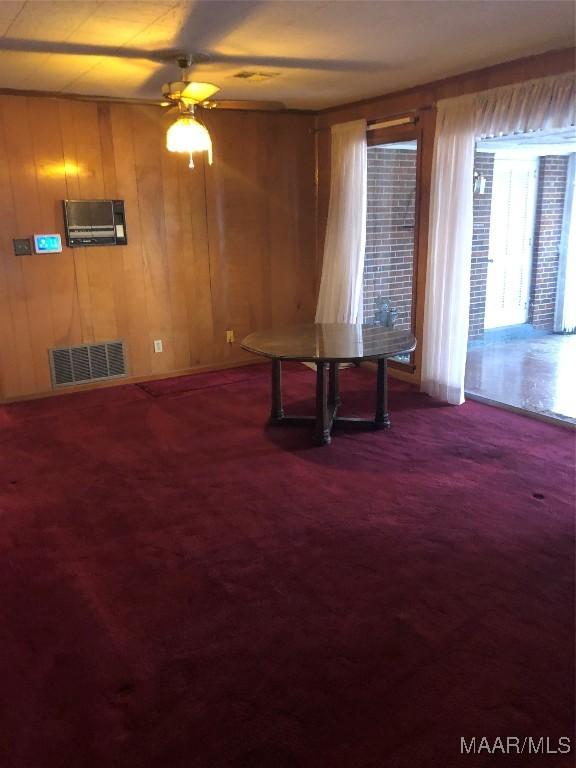 unfurnished dining area featuring ceiling fan, wooden walls, and dark colored carpet