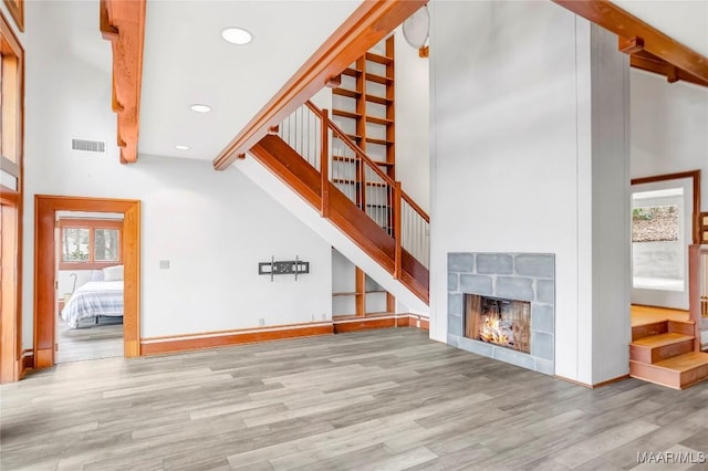 unfurnished living room featuring a towering ceiling, light hardwood / wood-style floors, and beamed ceiling