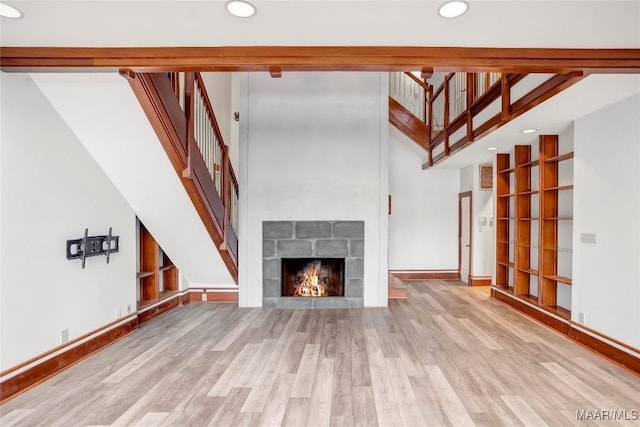 unfurnished living room featuring a stone fireplace, a high ceiling, and light wood-type flooring